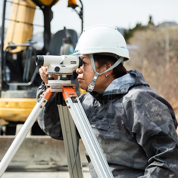 土木工事現場で、建築現場測量レベルを使い測量をしている職人の男性
